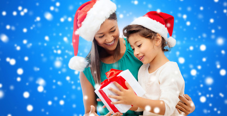 happy mother and girl in santa hats with gift box