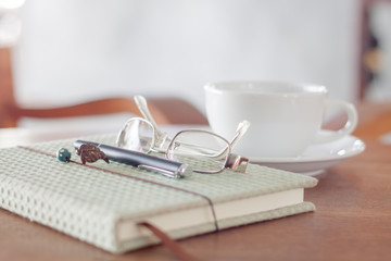 Notebook with pen, eyeglasses and white coffee cup