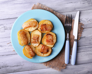 Baked potato with bacon on plate, on wooden background