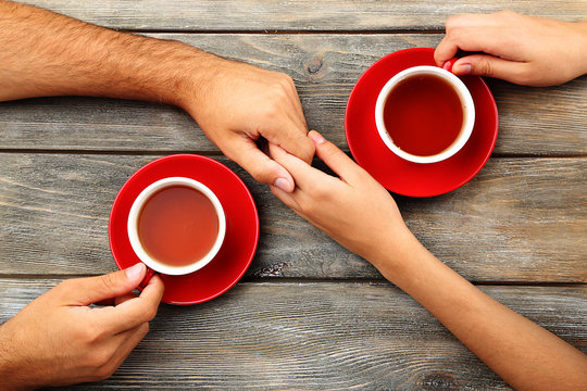 Tea cups and holding hands at the wooden table