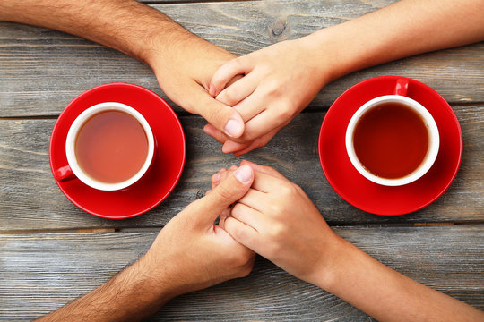 Tea cups and holding hands at the wooden table