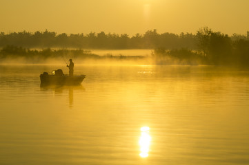 wędkarz na łodzi łowiący ryby w rzece pośród mgieł - obrazy, fototapety, plakaty