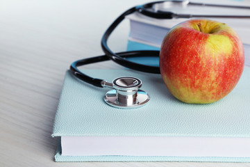 Medical stethoscope with apple on books on wooden table