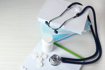 Medical stethoscope with books and tablet on wooden table