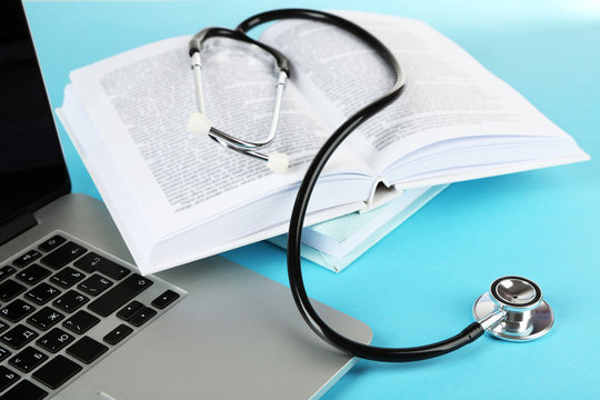 Medical stethoscope with books and laptop on blue background