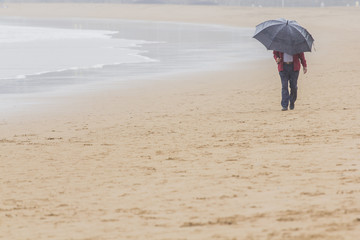 hombre con paraguas paseando por la playa