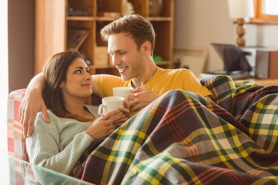 Young Couple Cuddling On The Couch Under Blanket