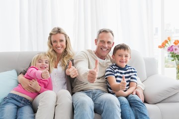 Happy family sitting on sofa giving thumbs up