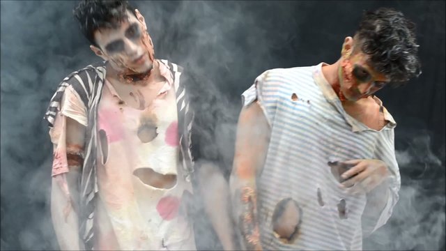 Two male zombies moving strangely. Dark background with smoke