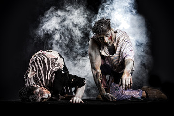 Two male zombies crawling on their knees, on dark background
