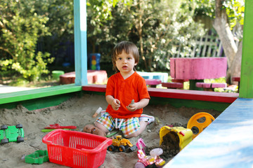 lovely boy playing with sand on playground in summer