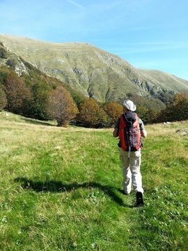 Escursista cammina su di un prato alle pendici di un monte