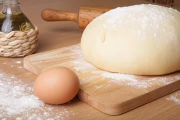 dough on a board with flour. olive oil, egg, rolling pin
