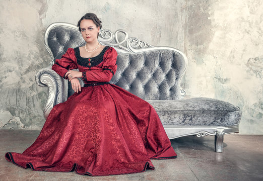 Beautiful woman in red medieval dress on the sofa