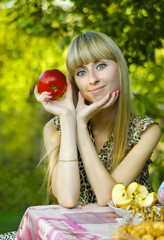 Девушка сидит за столом в саду, с яблоком в руках