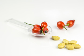 Rose hip on a medicine spoon with vitamine pills