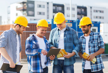 group of smiling builders with tablet pc outdoors