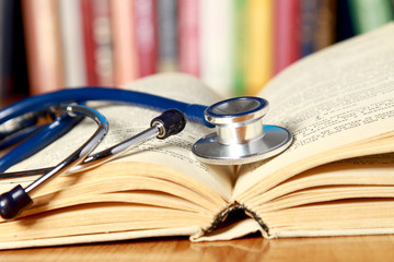 A stethoscope is lying with a book on the desk against books