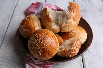 Tasty buns with sesame on plate, on color wooden background