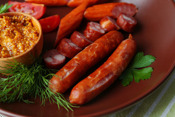 Assortment of tasty thin sausages on plate on wooden background