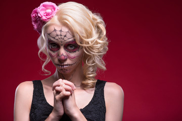 Portrait of young blond girl with Calaveras makeup and a rose fl