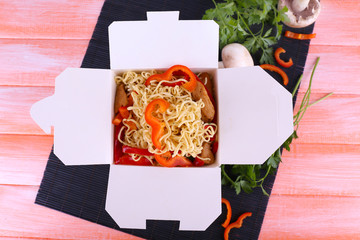 Chinese noodles in takeaway box on black mat on pink background