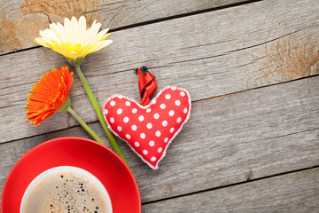 Cup of coffee, heart toy and gerbera flowers on wooden table