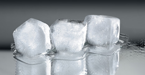 Three ice cubes with reflection on grey gradient background.