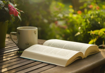 Fototapeta premium Cup of tea and open book on wooden table in garden.