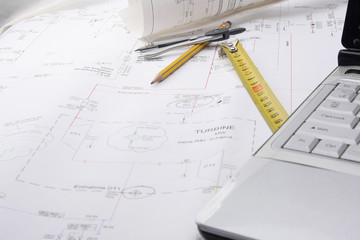 A ruler, a pencil, dividers and a laptop on a draft