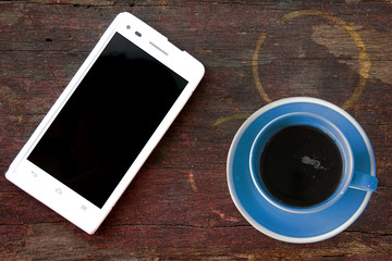 Mobile phone and coffee cup on office wooden table