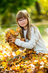 Pretty young girl sitting on colorful autumn leaves.