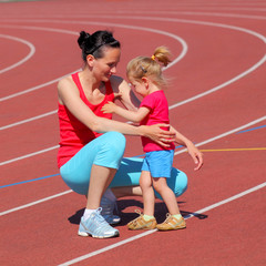 Mother and little daughter are running in the stadium.