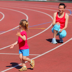 Mother and little daughter are running in the stadium.