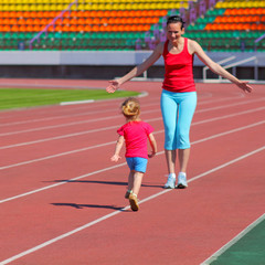 Obraz premium Mother and little daughter are running in the stadium.