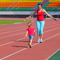 Mother and little daughter are running in the stadium.