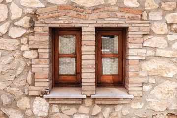 Fototapeta na wymiar Old stone wall with two small windows in wooden frames