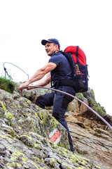 Young man hiking on difficult mountain trail with hanging cable