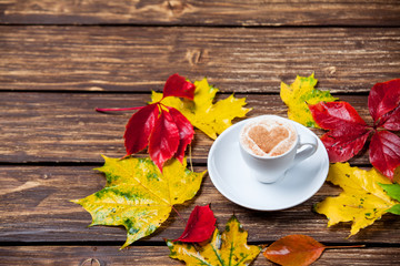 Autumn leafs and coffee cup on wooden table.