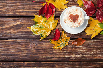 Autumn leafs and coffee cup on wooden table.