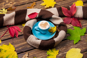 Autumn leafs, scarf and coffee cup on wooden table.