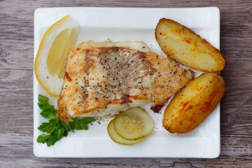 White fish with potato wedges on white plat, woodeen background