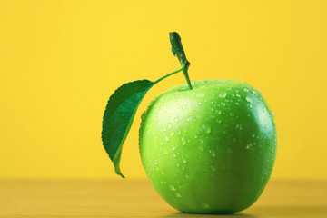 Green apple with water drops on yellow background