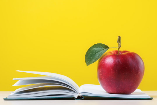 Red apple with green leaf on open notebook