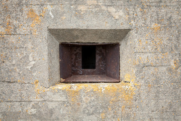 Rusted loophole in old concrete bunker wall