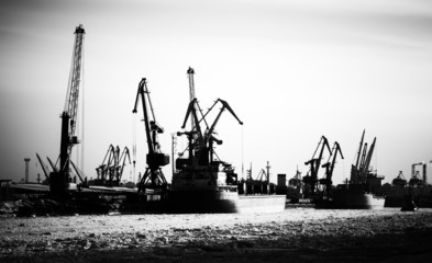 Silhouettes of cargo port skyline with cranes, ships and poles