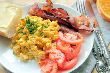 Breakfast with scrambled eggs, bacon, tomatoes and fresh orange