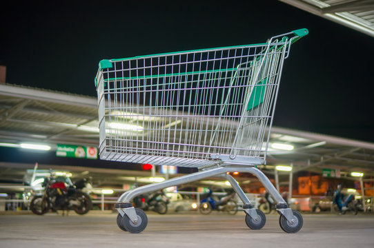 Empty shopping cart with green handle on parking near supermarke