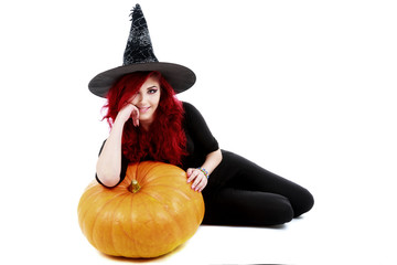 redhead witch sits leaning against a big pumpkin