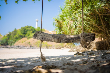 Rope swing on tropical island beach with lighthouse on back